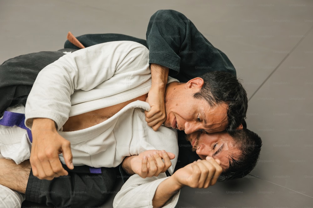 two men in white shirts and black pants are wrestling