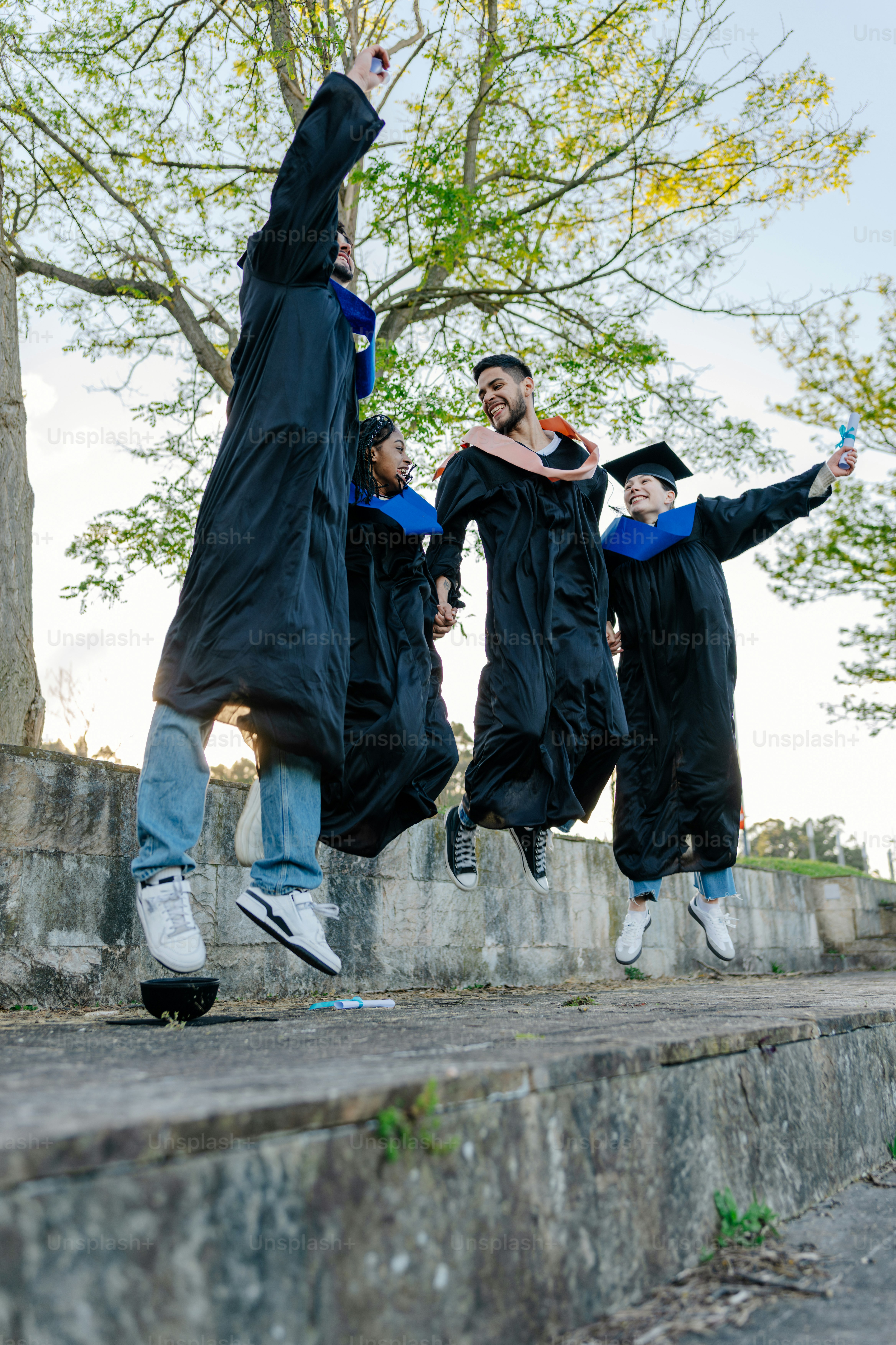 Graduates in caps and gowns jumping with joy outdoors