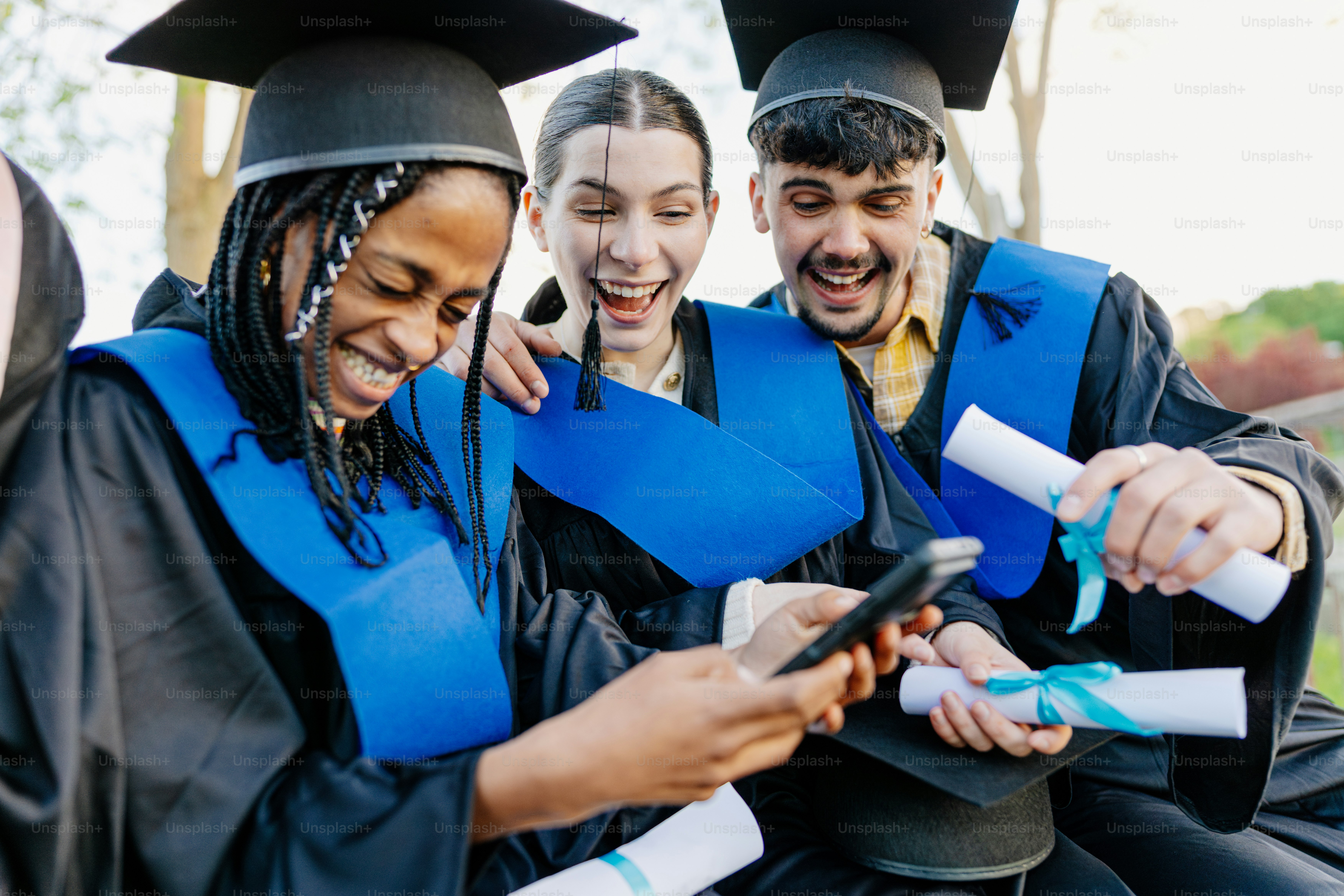Formandos de toga e gorro olham para um smartphone