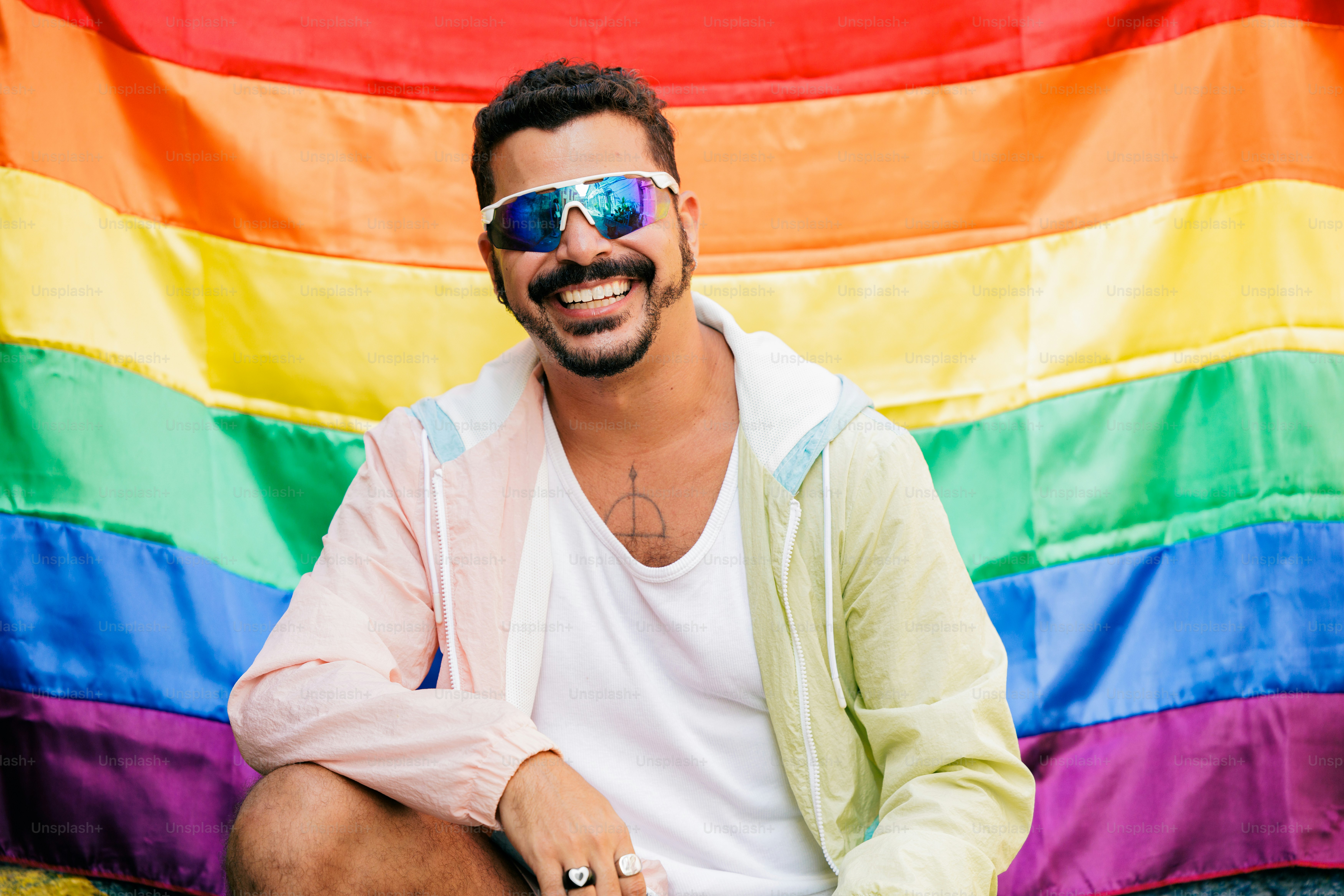 um homem sentado em frente a uma bandeira do arco-íris