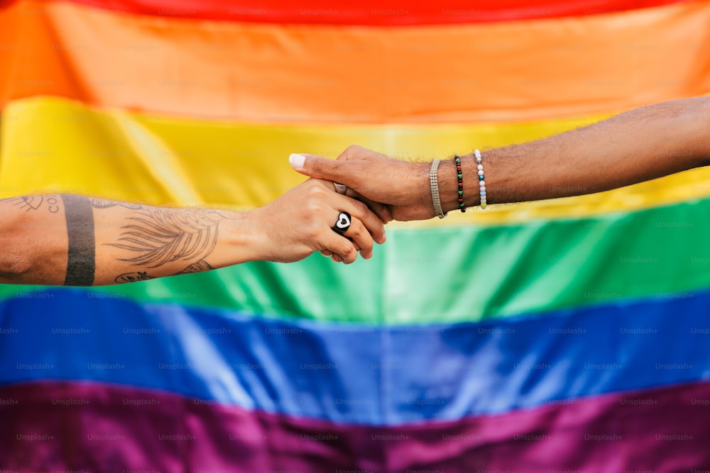 a man and a woman holding hands in front of a rainbow flag