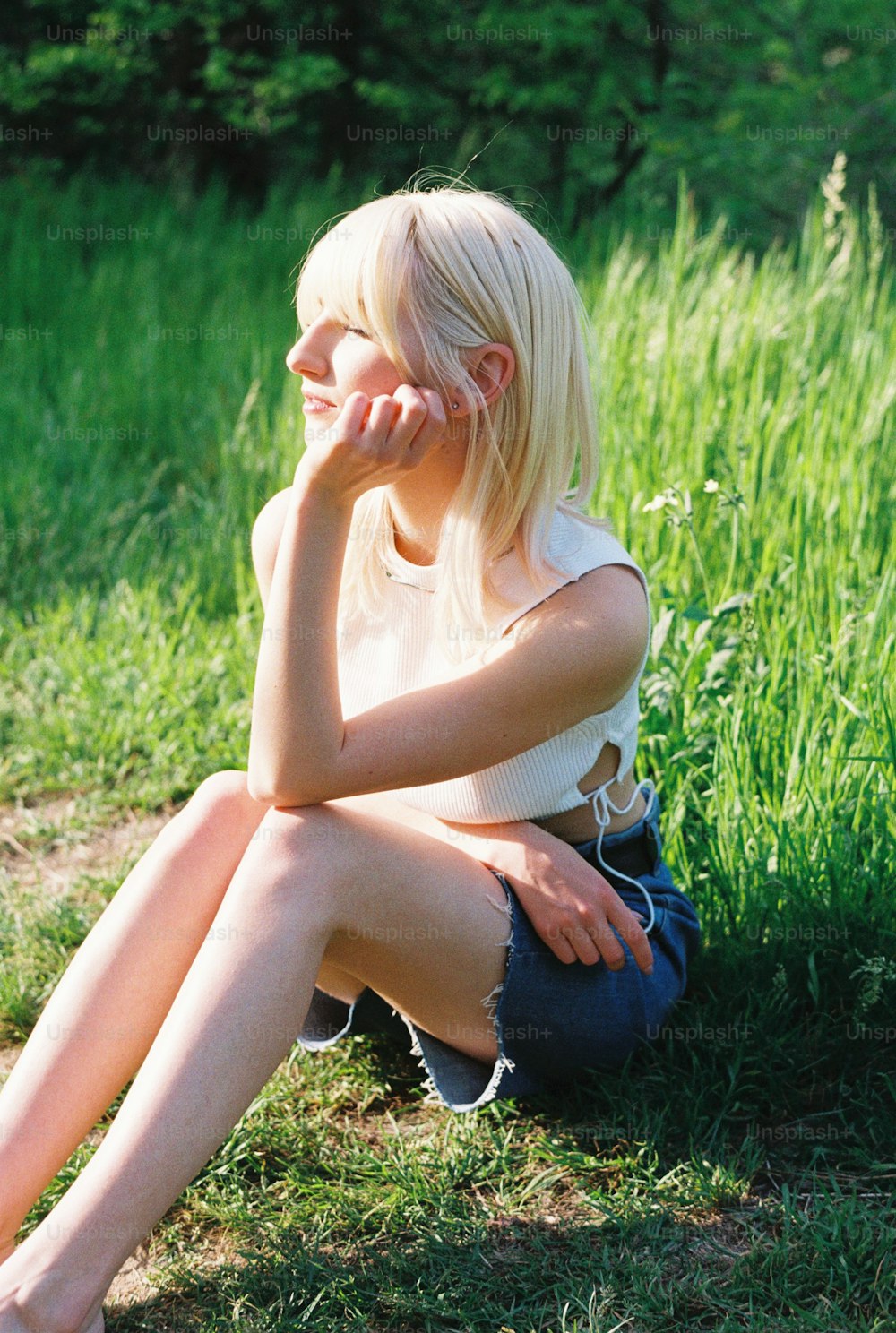 uma mulher sentada na grama com a mão no rosto