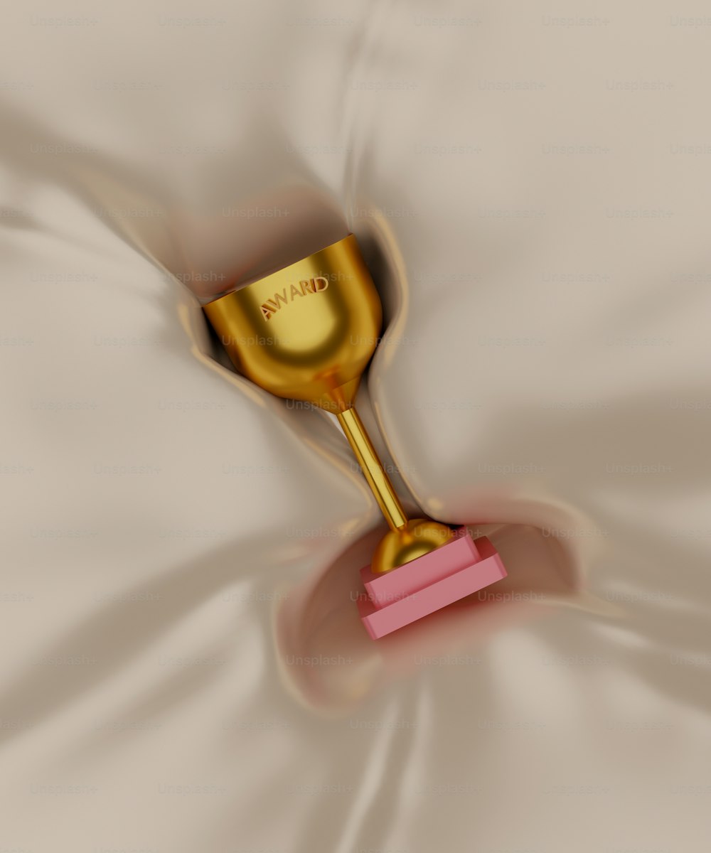 a gold cup with a pink handle on a white sheet