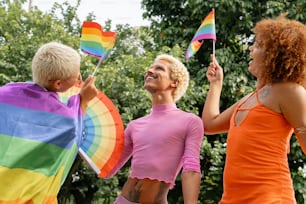 um grupo de pessoas em pé ao redor umas das outras segurando bandeiras do arco-íris