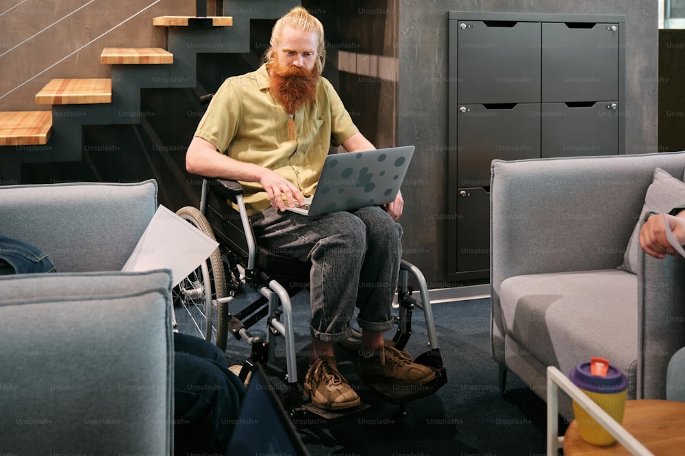 Un hombre sentado en una silla de ruedas usando una computadora portátil