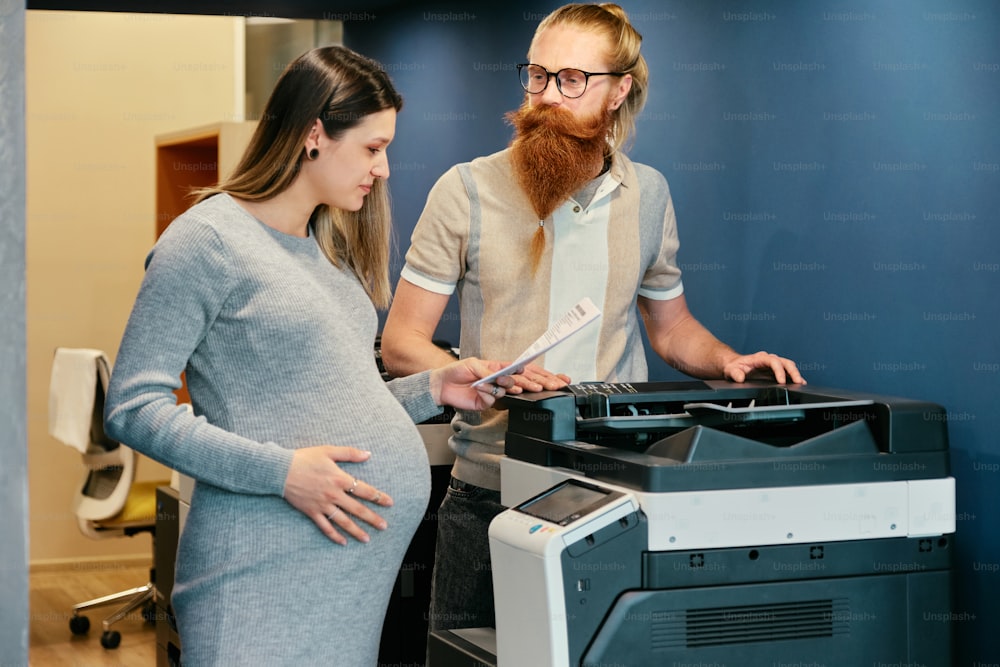 a pregnant woman standing next to a man in front of a printer
