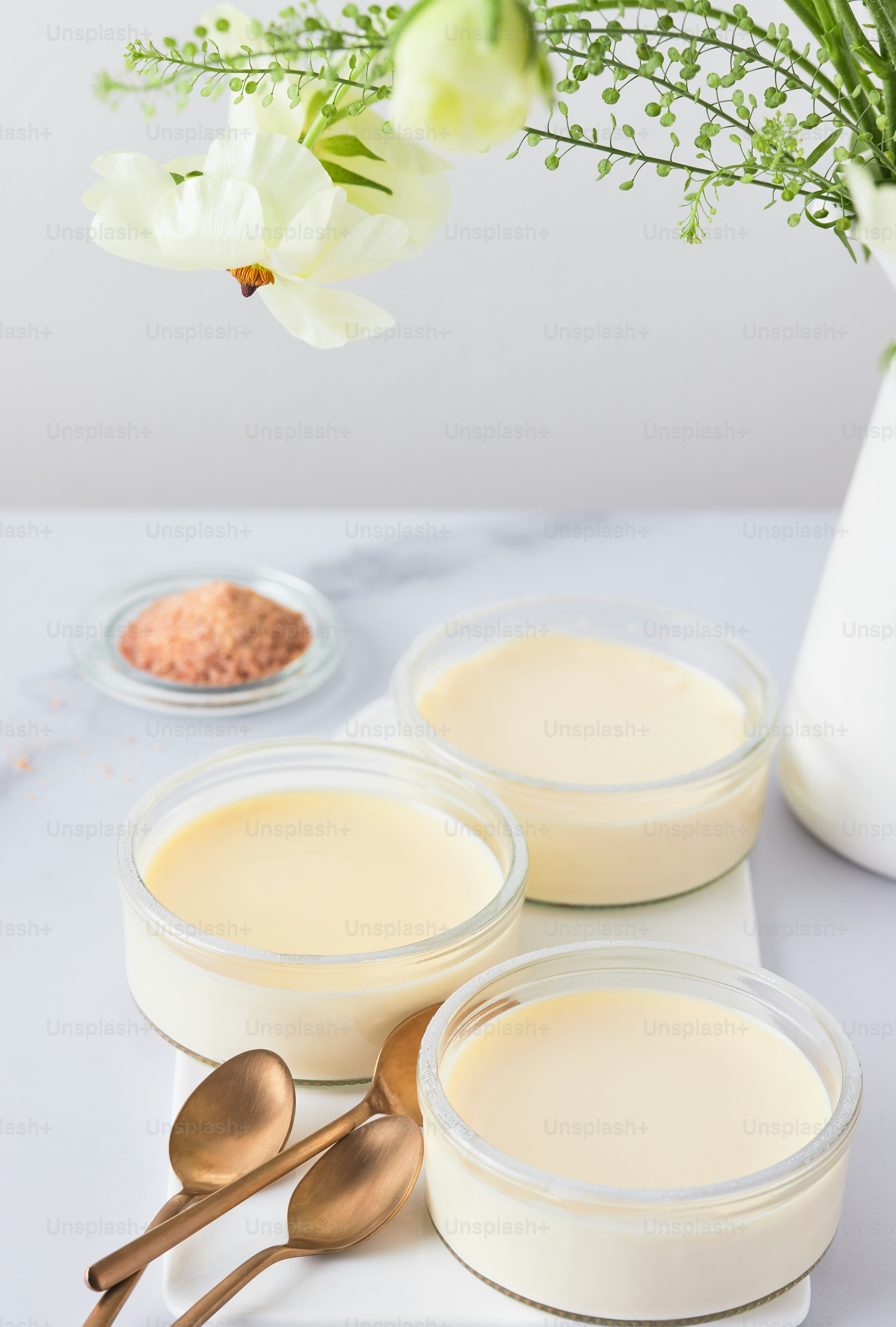 three bowls of yogurt with spoons and a vase of flowers