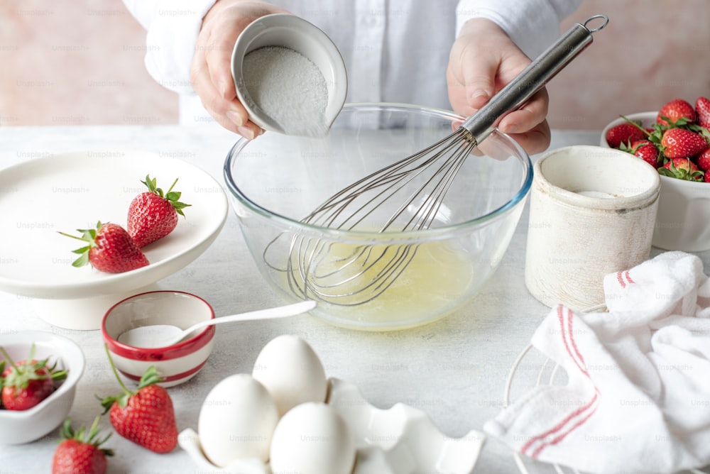 une personne fouettant des œufs et des fraises dans un bol