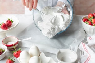 a person mixing whipped cream in a bowl with strawberries