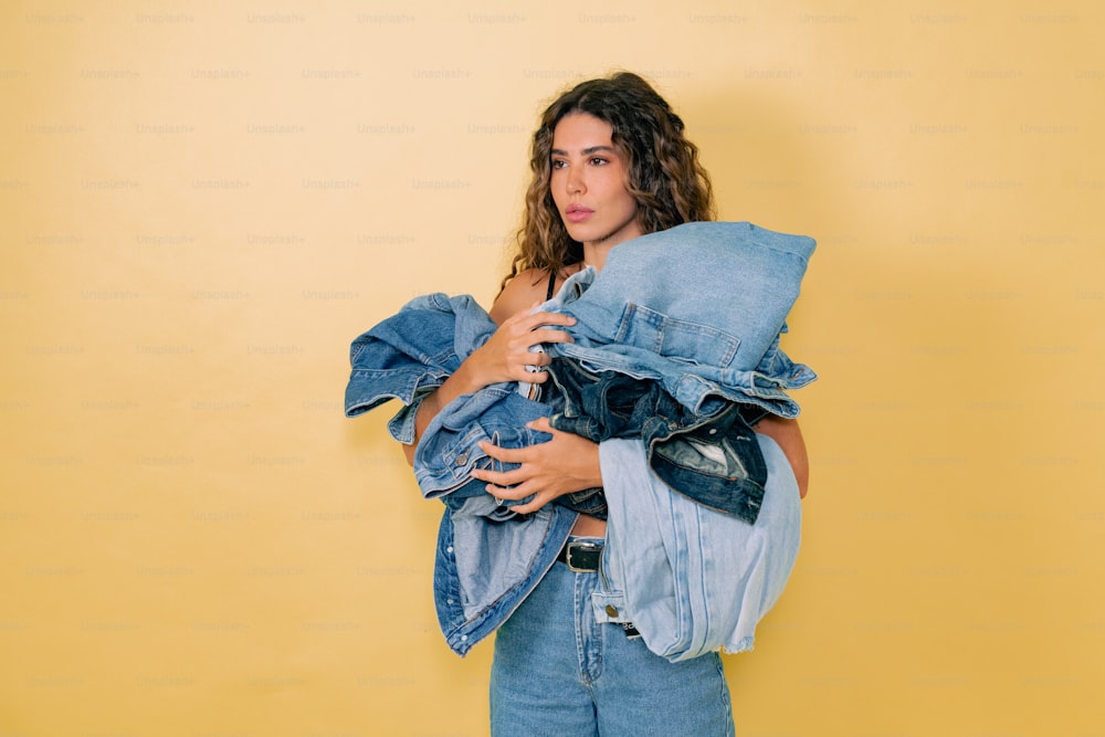 a woman holding a pile of clothes in front of a yellow wall