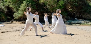 a group of women in white dresses dancing on a beach