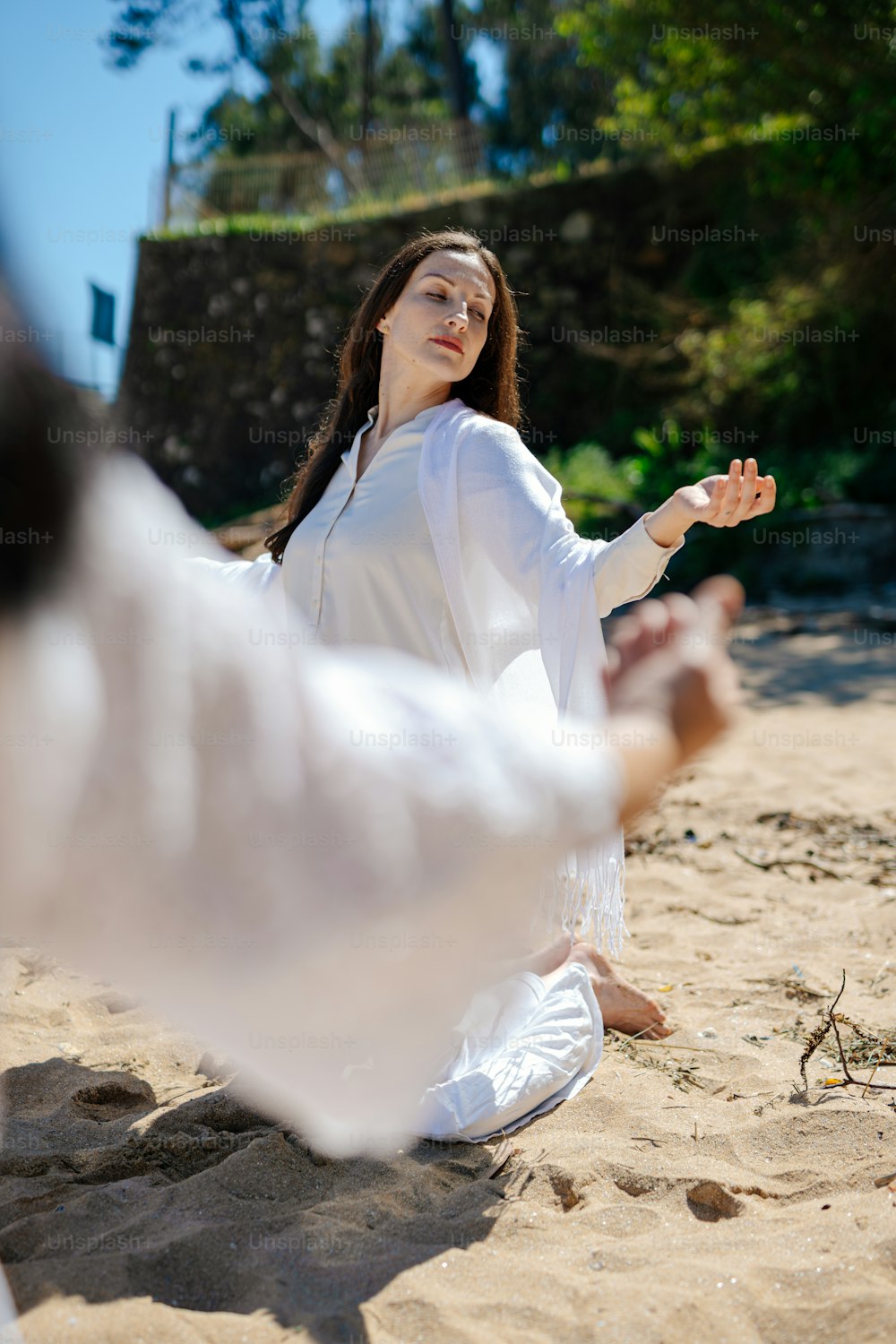eine Frau in einem weißen Kleid sitzt am Strand