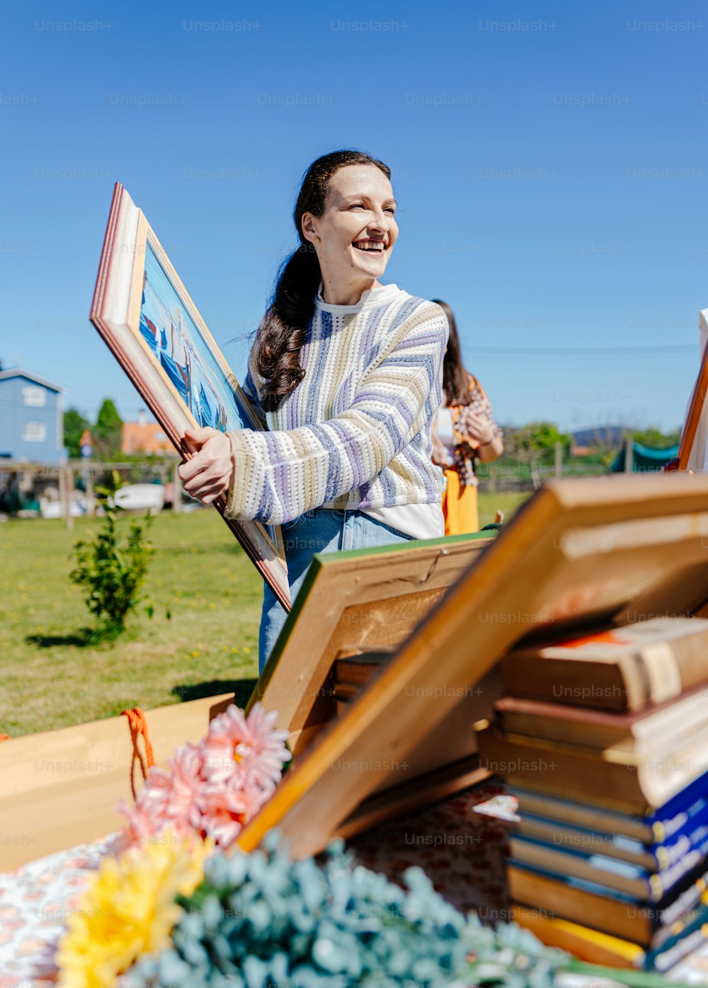 a woman holding up a picture frame in front of a pile of books