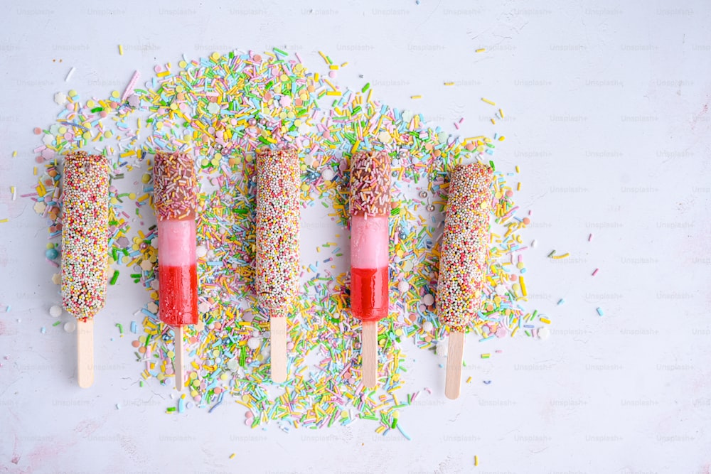 four popsicles with sprinkles on them on a white surface