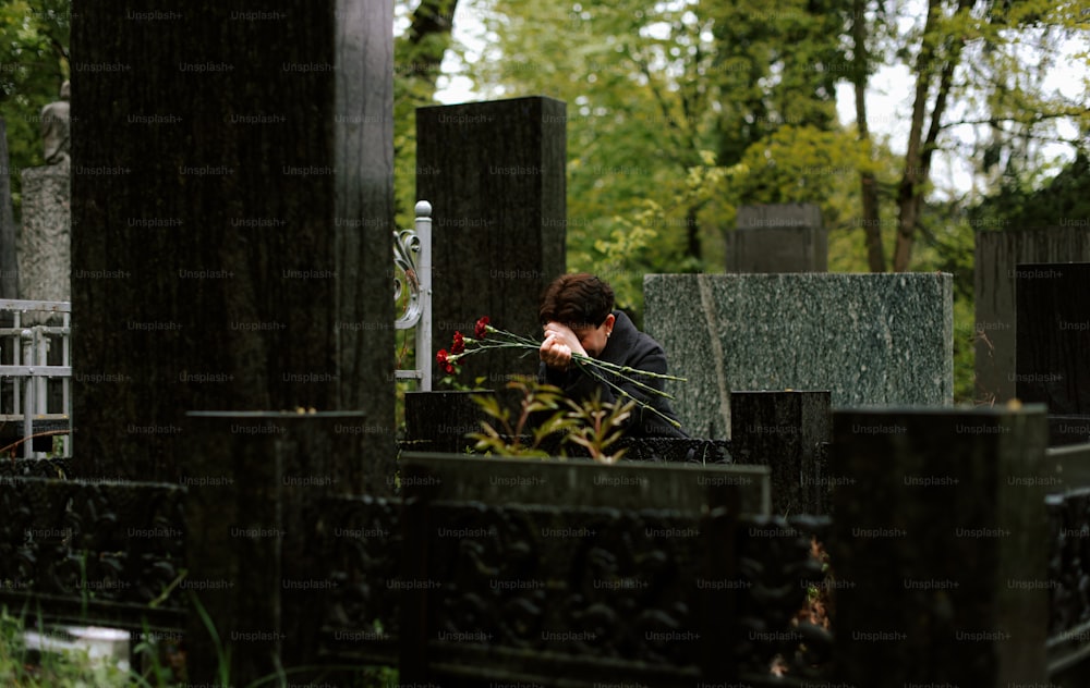 uma mulher sentada em um cemitério com as mãos no rosto