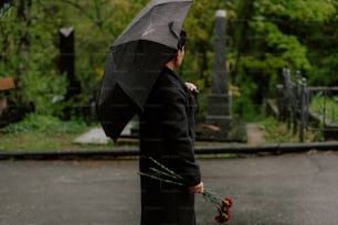 Eine Frau in einem schwarzen Mantel hält einen schwarzen Regenschirm in der Hand