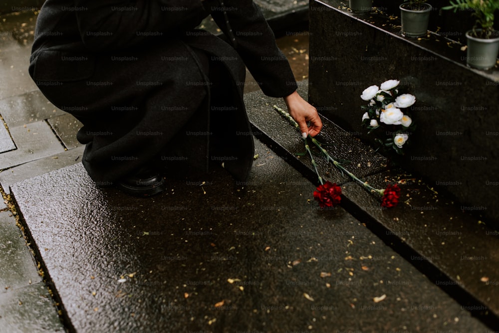 una persona inginocchiata accanto a un mazzo di fiori
