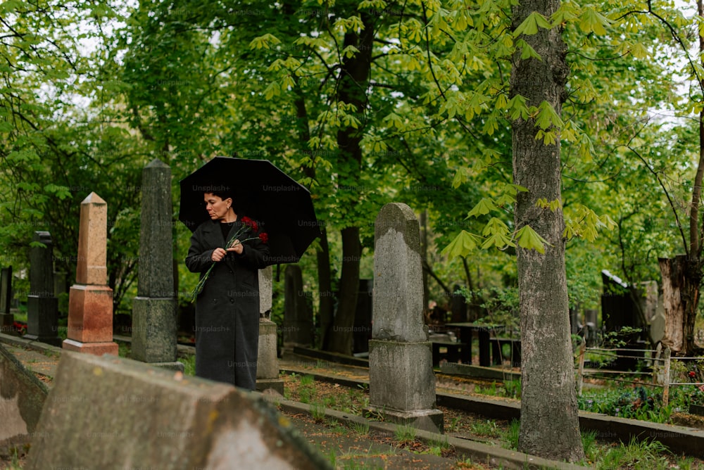a woman standing in a cemetery holding an umbrella