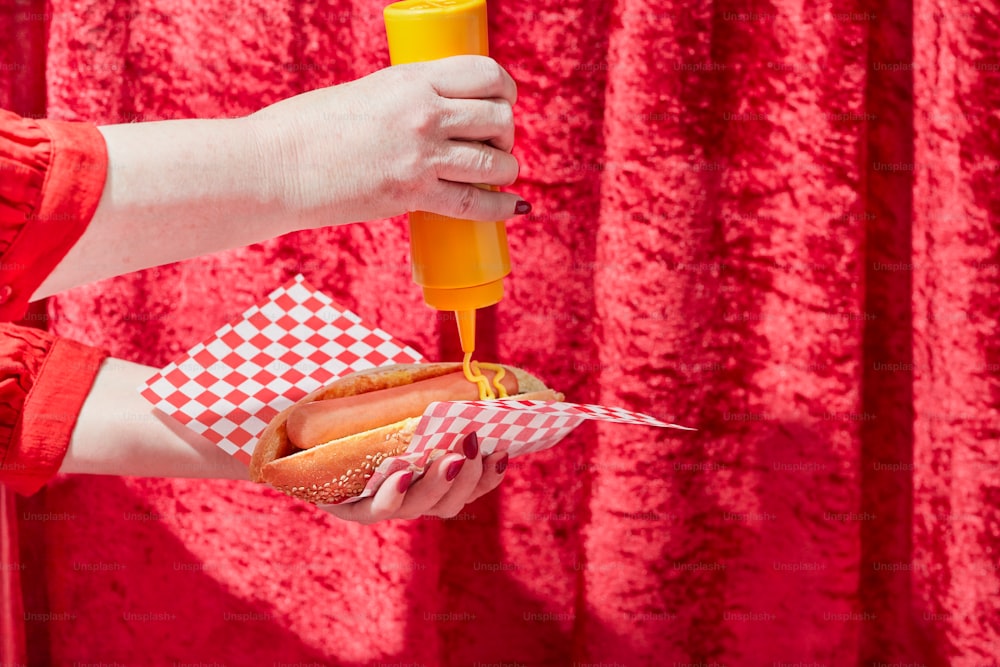 a person holding a hot dog in a bun with mustard and ketchup