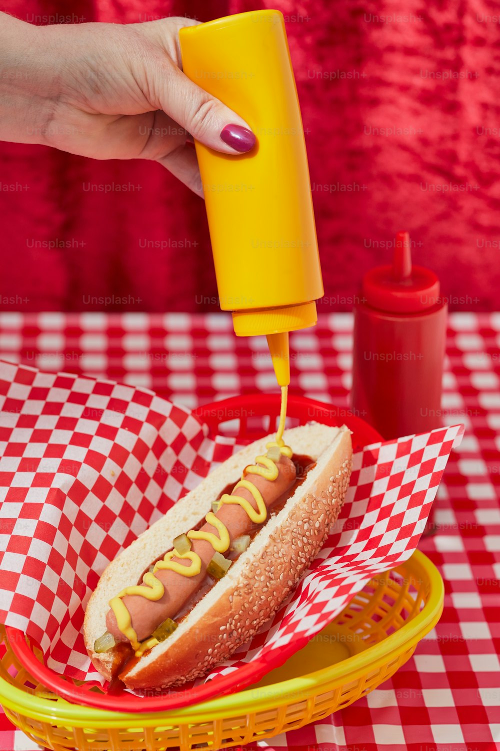 a hot dog in a basket with mustard being drizzled on it