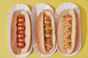 trois hot-dogs à la moutarde et au ketchup dans des assiettes en carton