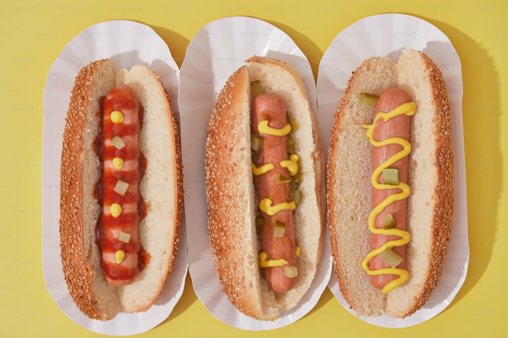 three hotdogs with mustard and ketchup in paper plates