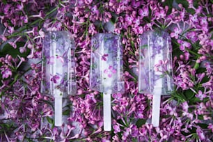 trois sucettes glacées avec des fleurs posées sur un lit de fleurs violettes