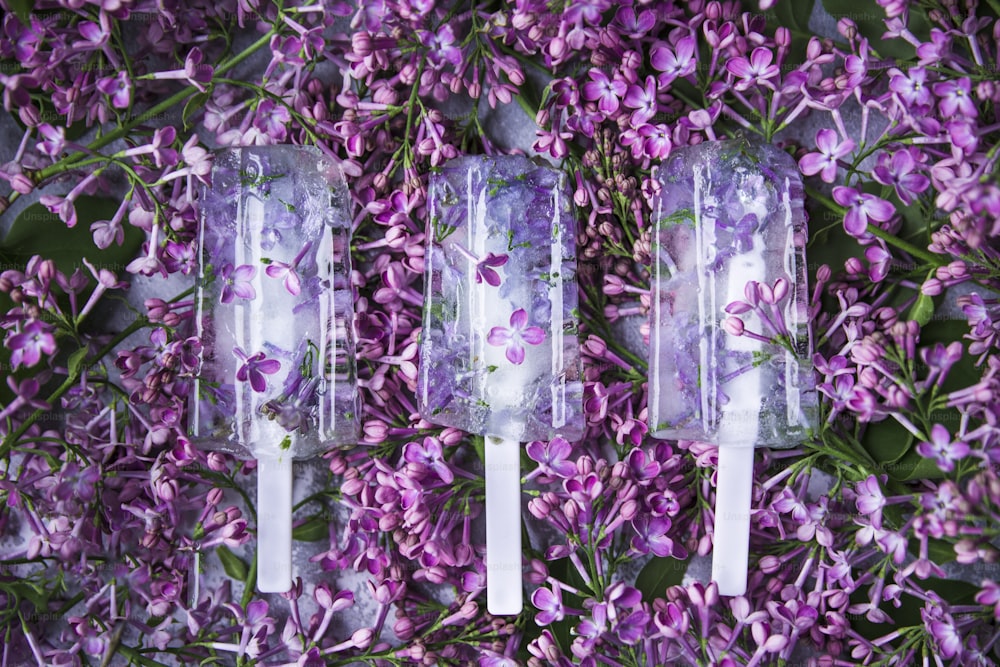 tre ghiaccioli con fiori su di loro seduti su un letto di fiori viola