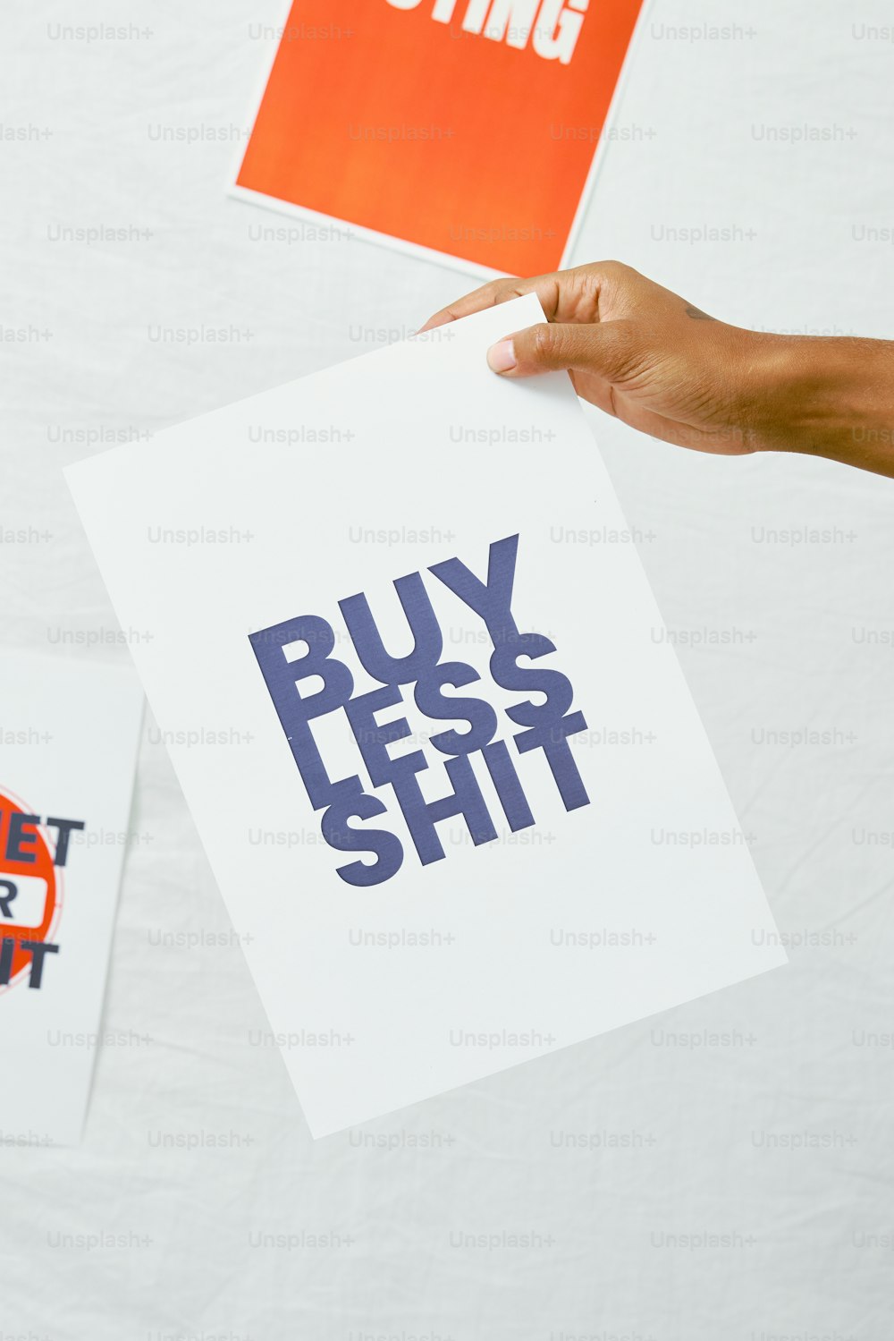 a person holding a piece of paper that says buy less shit
