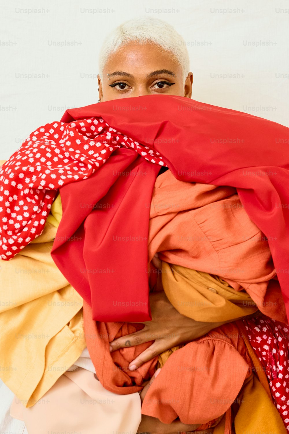 a woman hiding her face behind a pile of clothes