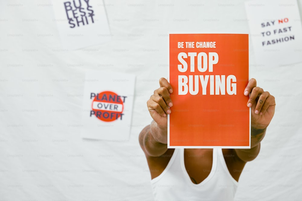 a woman holding up a sign that reads be the change stop buying