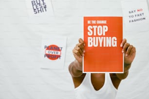 a woman holding up a sign that reads be the change stop buying