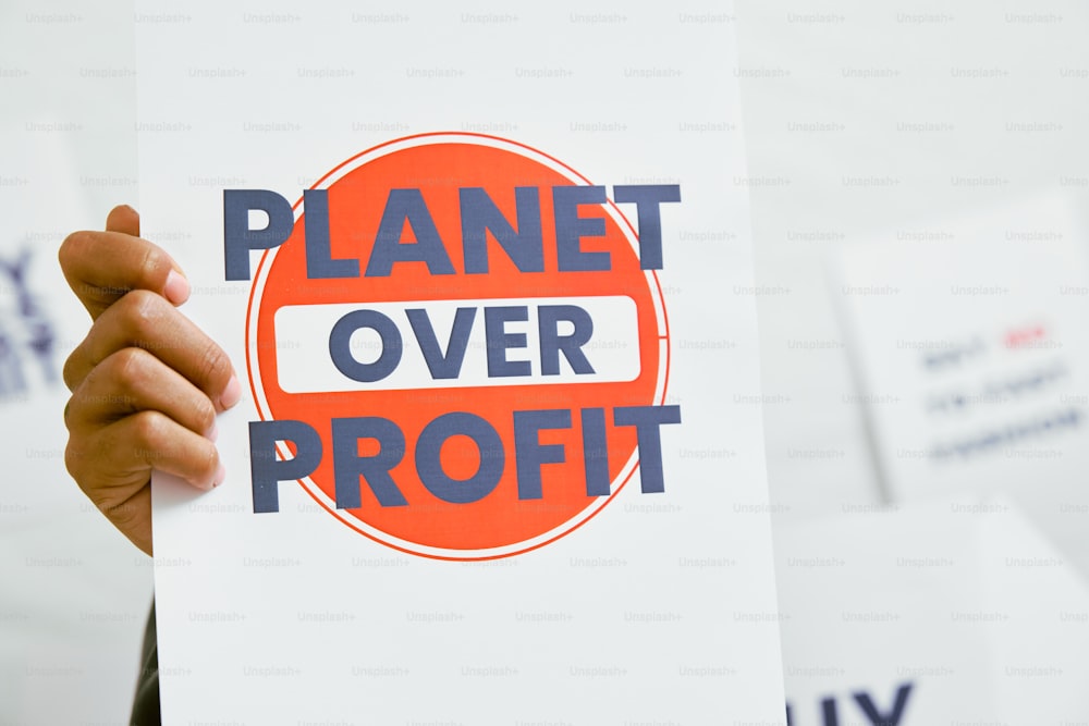 a person holding a sign that says planet over profits