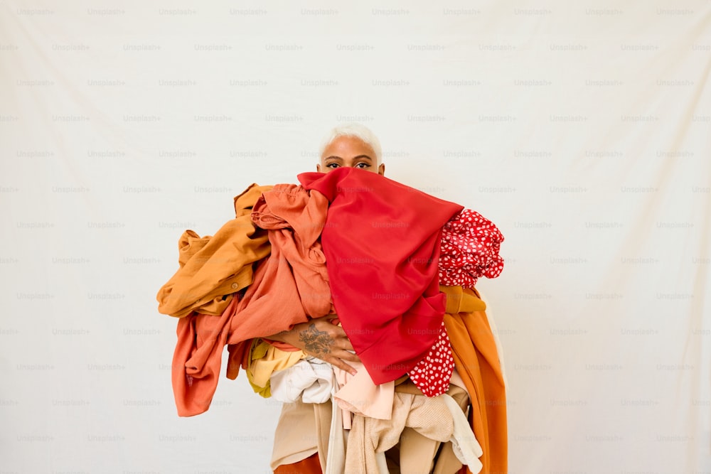 uma mulher segurando uma pilha de roupas na frente de um fundo branco