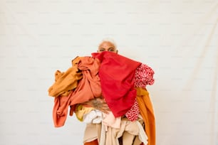 eine Frau hält einen Haufen Kleidung vor weißem Hintergrund