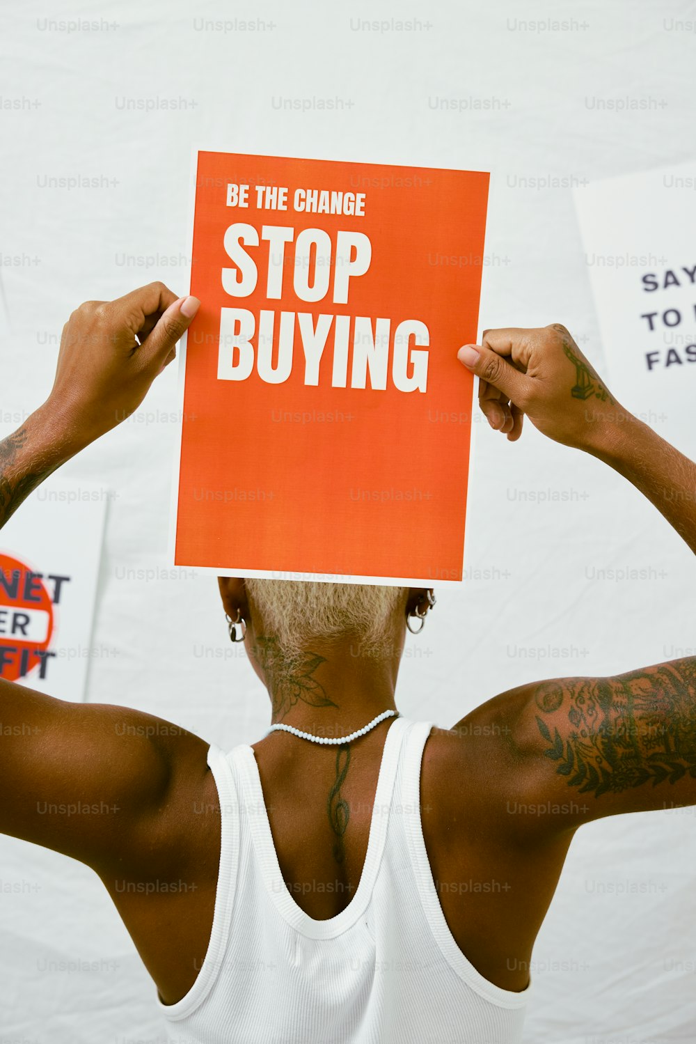 a man holding a sign that says be the change stop buying