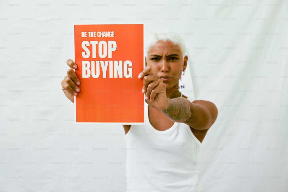 a man holding a sign that says be the change stop buying