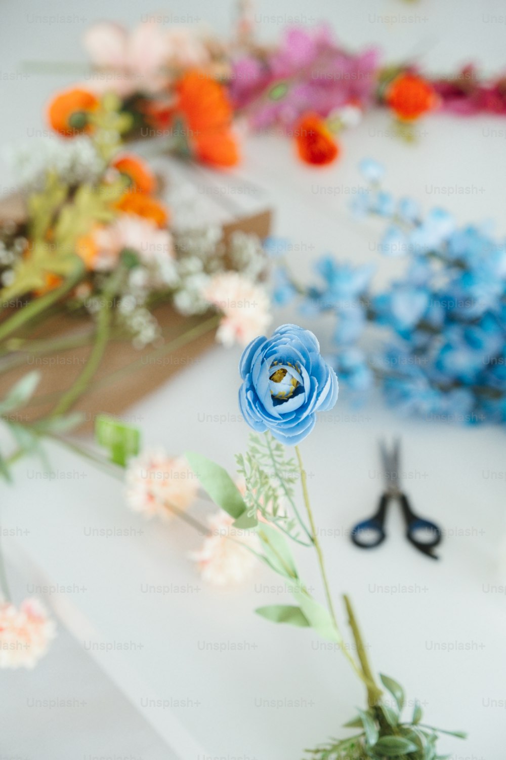 una flor azul sentada encima de una mesa junto a unas tijeras