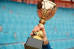 uma pessoa segurando um troféu em frente a um estádio