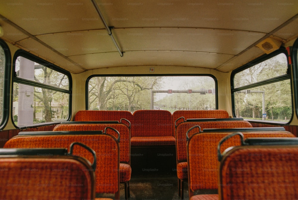 Un autobús vacío con asientos naranjas y árboles al fondo