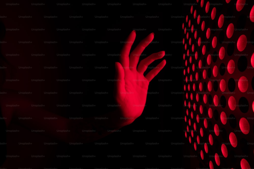La mano de una persona tocando una pared con luces rojas