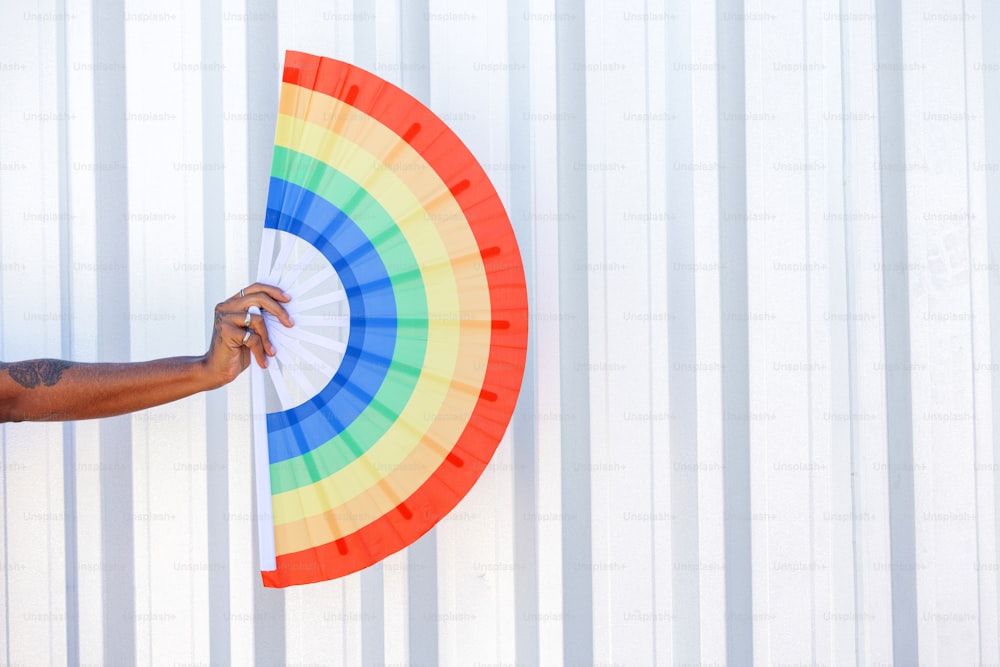 a person holding a colorful fan against a white wall