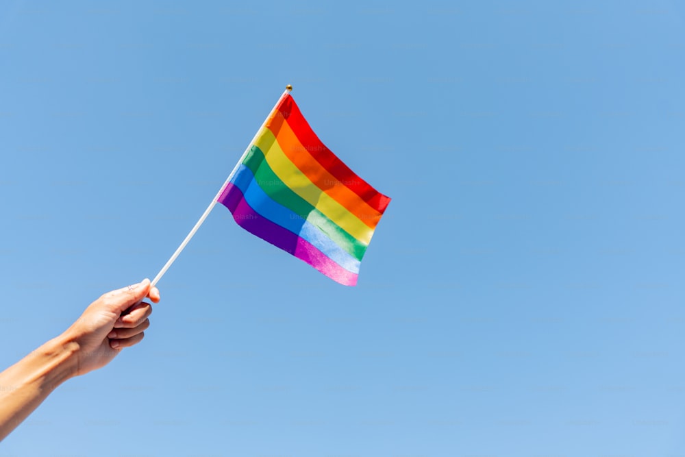 a hand holding a rainbow flag against a blue sky