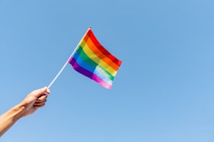 a hand holding a rainbow flag against a blue sky