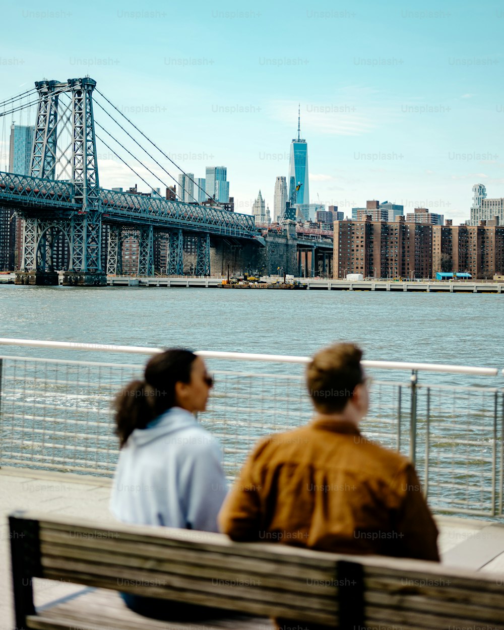two people sitting on a bench looking at a bridge