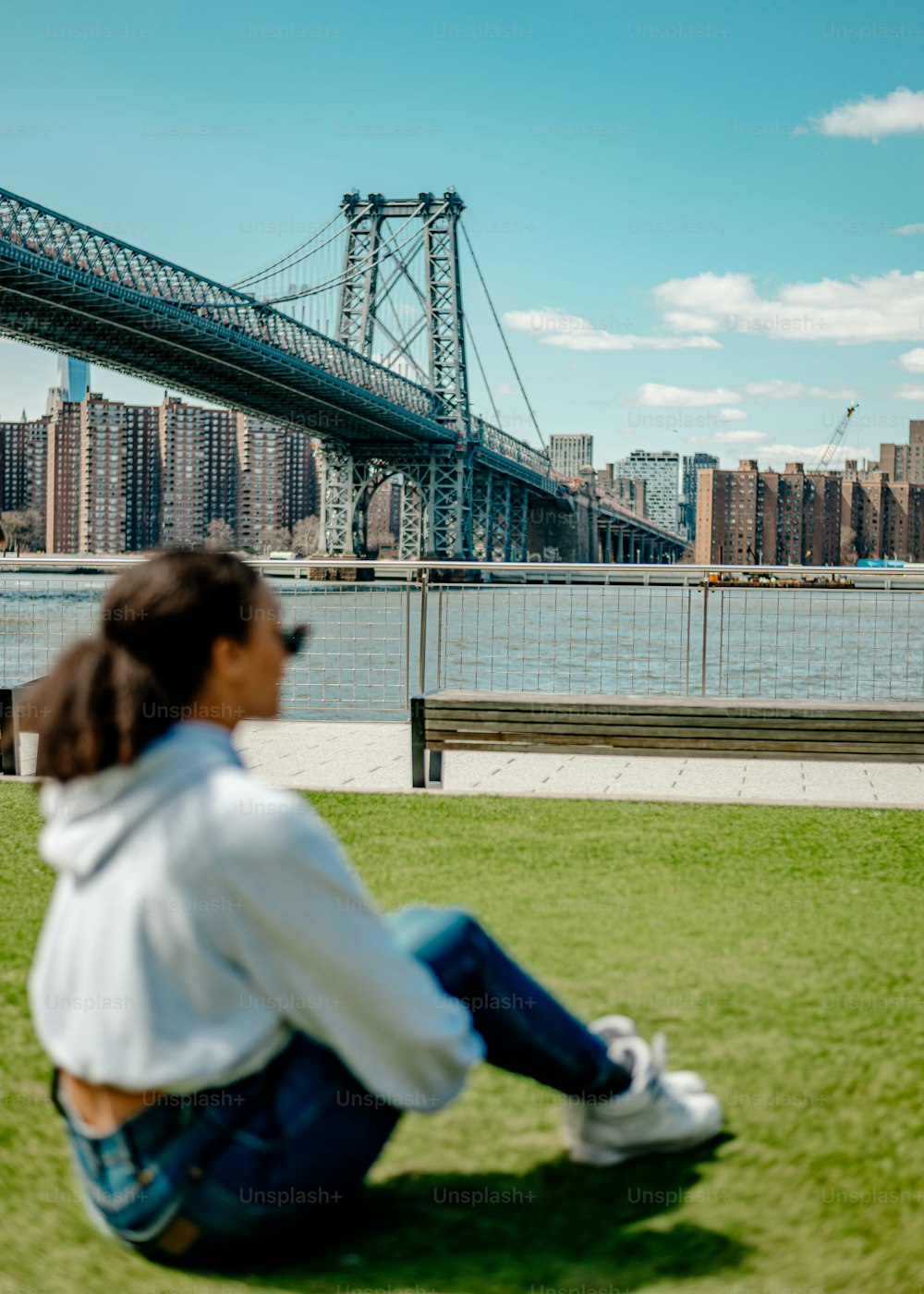 a woman sitting on the grass in front of a bridge