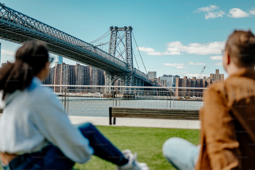 un homme et une femme assis sur un banc devant un pont