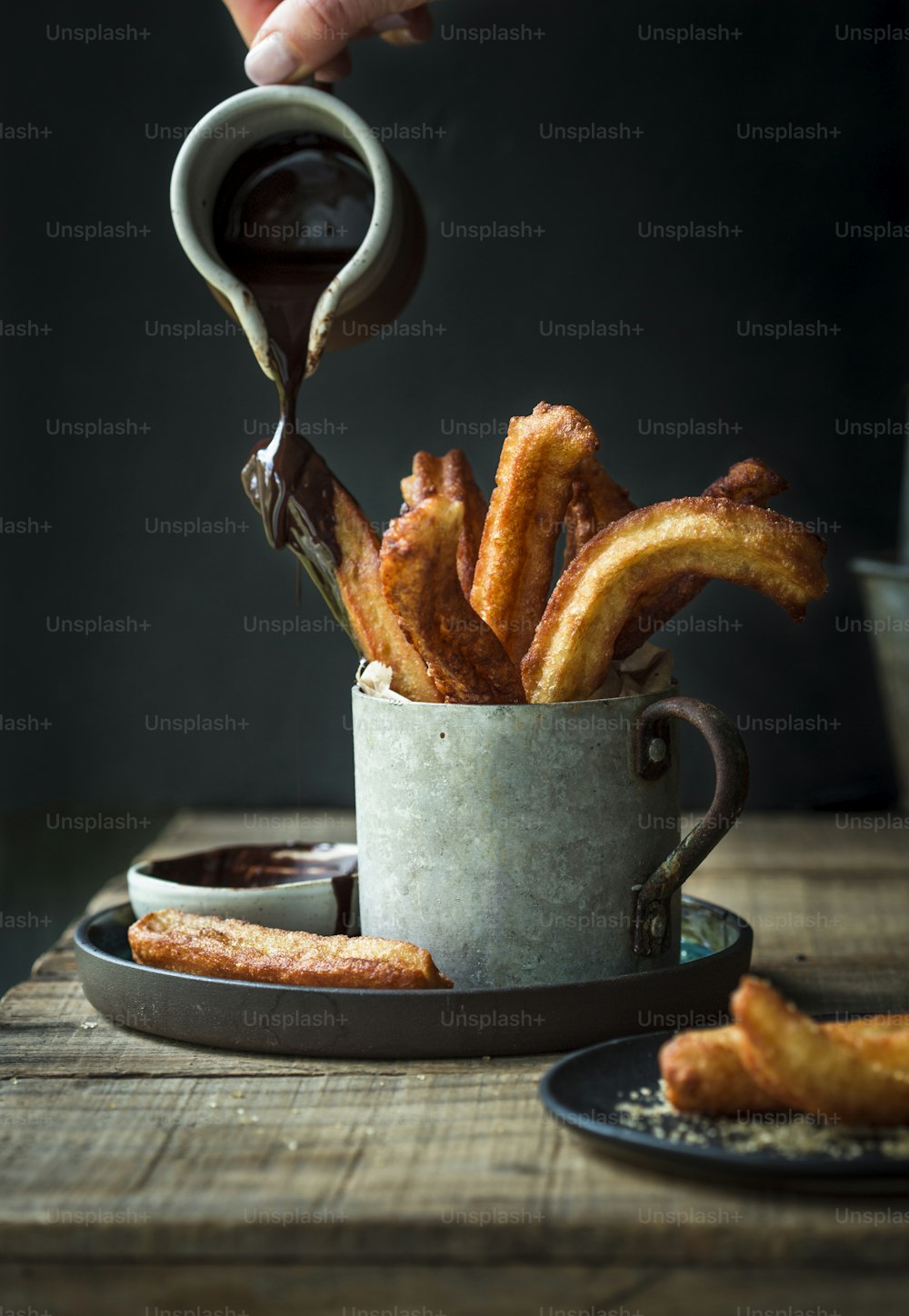 a person pouring chocolate into a cup of churros