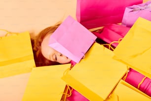 a little girl laying on top of a pile of yellow and pink bags