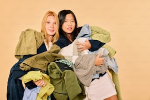 two women standing next to each other holding clothes
